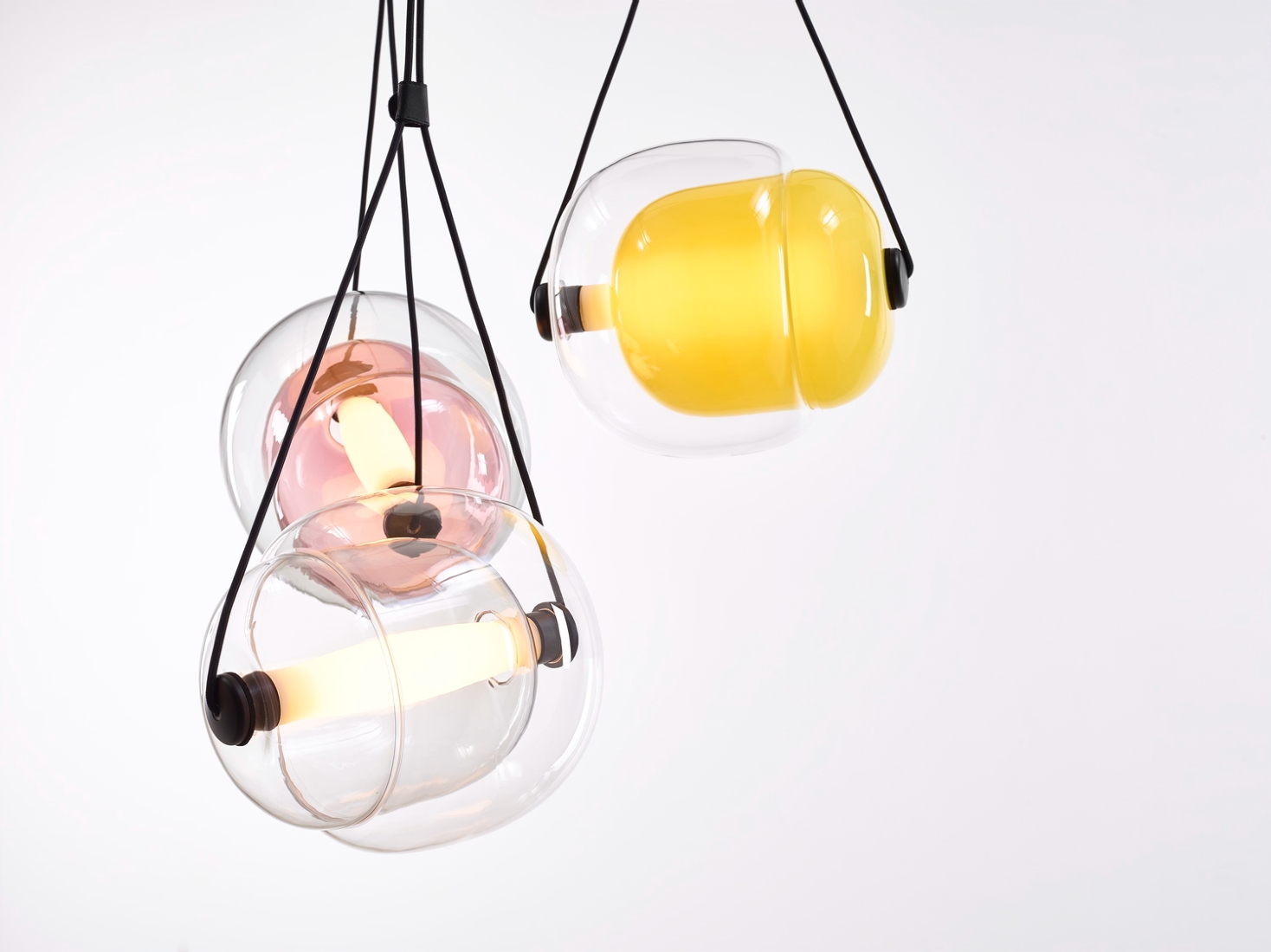 Three Brokis Capsula pendants with handblown glass - clear, violet, yellow -suspend elegantly from black cords.