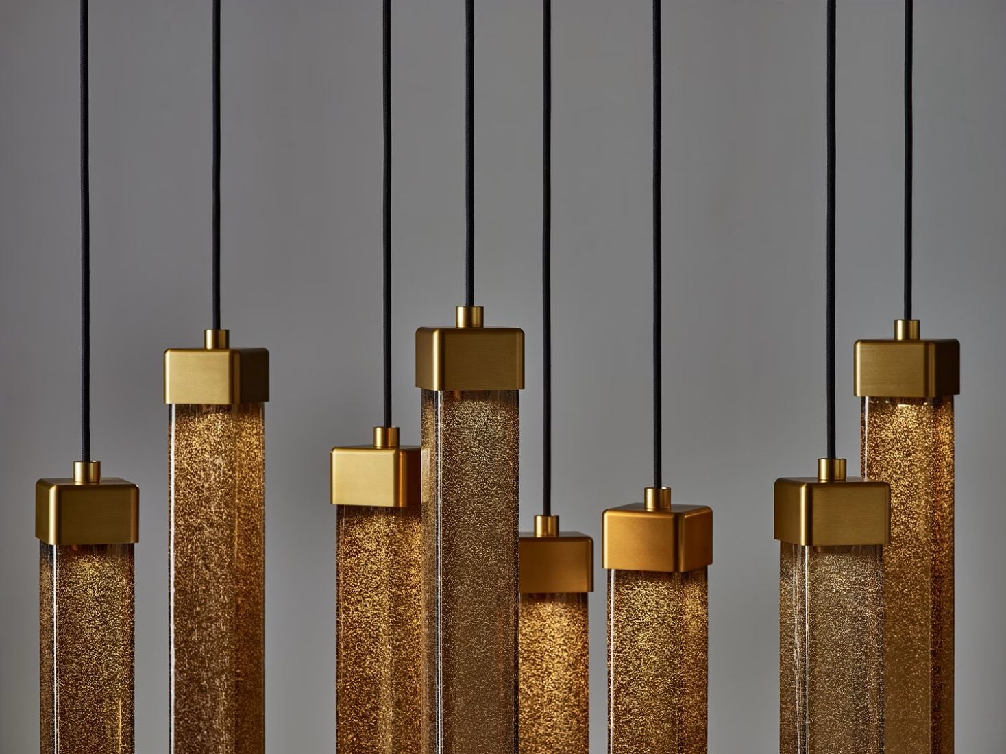 Close-up of Brokis Comet Square pendant lights with gold-toned tops and handblown glass, suspended elegantly on black cords.