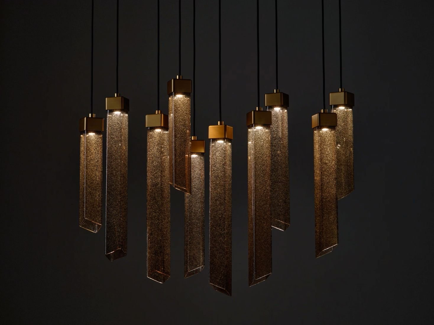 Brokis Comet Square pendant lights with silica glass and brass caps cast a warm, luxurious glow against a dark backdrop.
