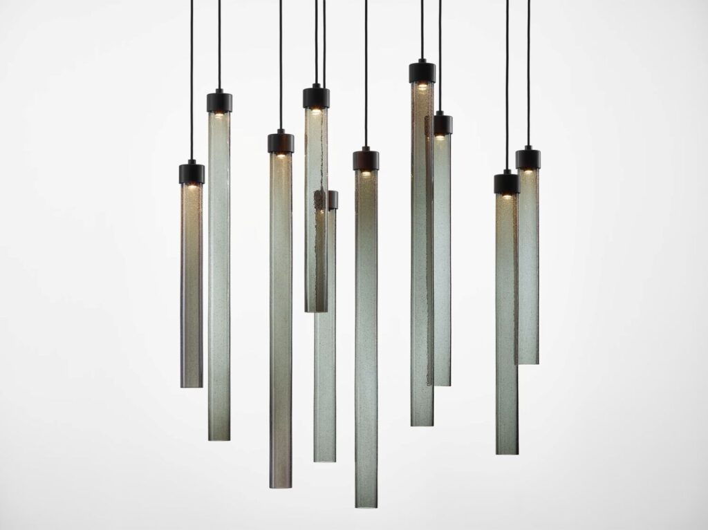 Ten Brokis Comet Round pendant lights hang at varied heights; glowing crystal tubes suspended by black cords.