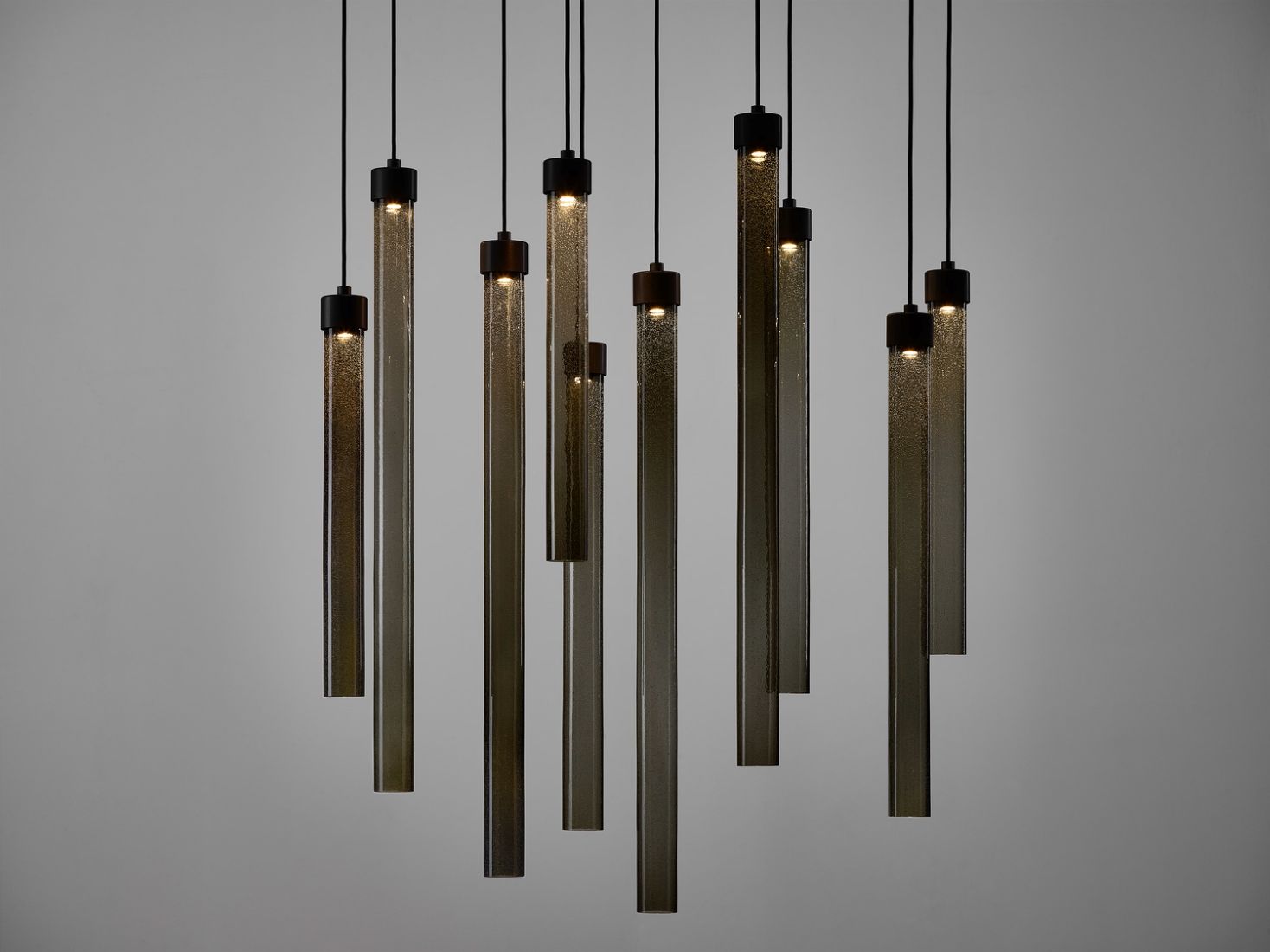 Brokis Comet Round glass pendant lights with visible bulbs glow at varied heights against a minimalist grey backdrop.
