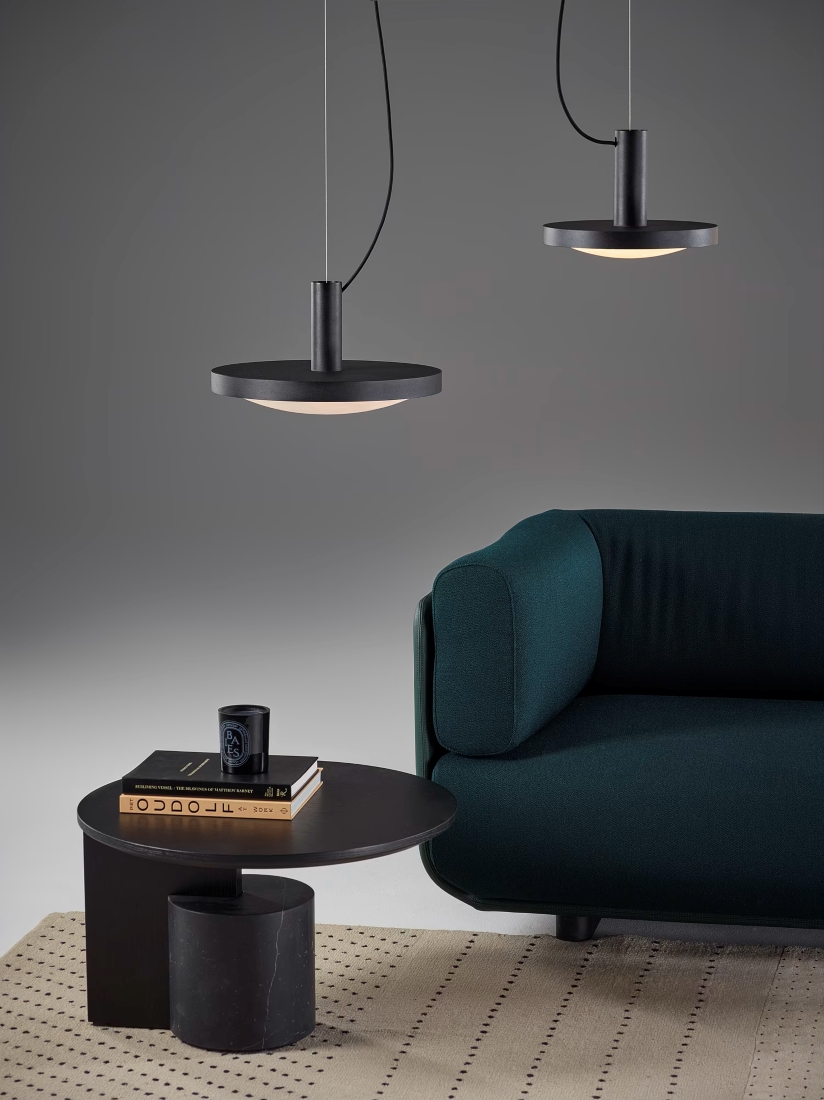 A modern living room with a dark green sofa, Brokis Convex Pendants, and a luxe black coffee table on a pale rug.