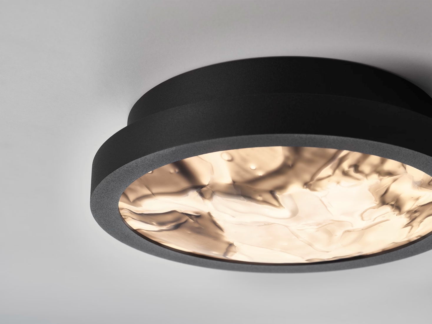 Brokis Convex S Applique ceiling light in black, its wavy glass diffuser glows warmly, casting rippling patterns overhead.