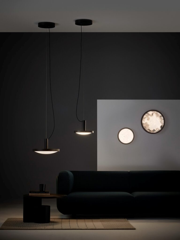 A chic living room with a dark sofa, Brokis Convex Pendant lights, Applique wall lights, as soft minimal lighting.