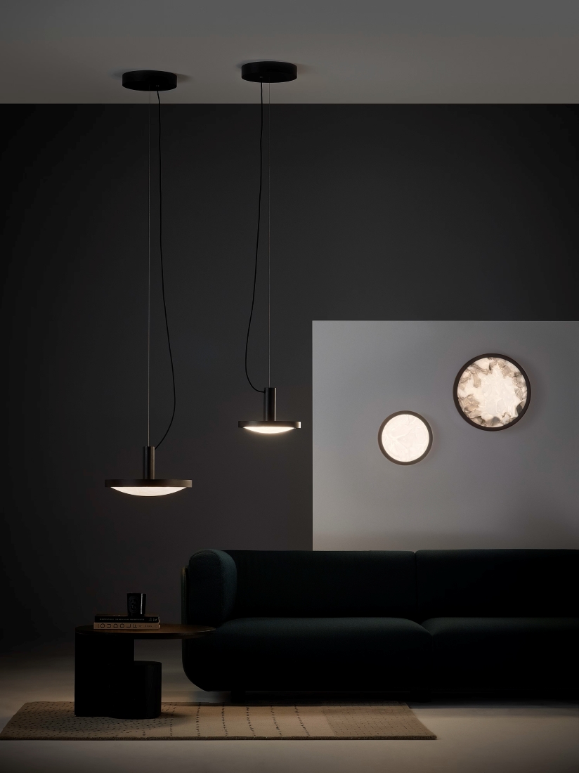 A chic living room with a dark sofa, Brokis Convex Pendant lights, Applique wall lights, as soft minimal lighting.