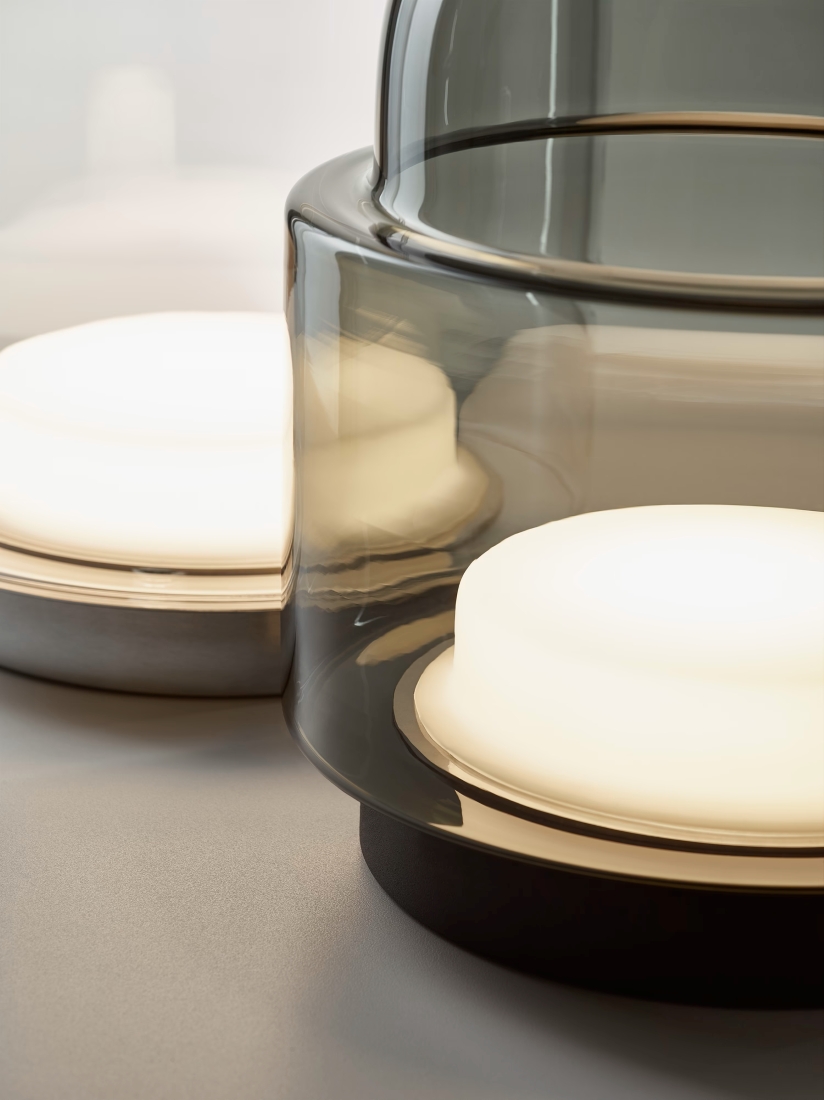 Close-up of two Brokis Dome table lamps in handblown glass, glowing warmly on a sleek grey surface; pure elegance.