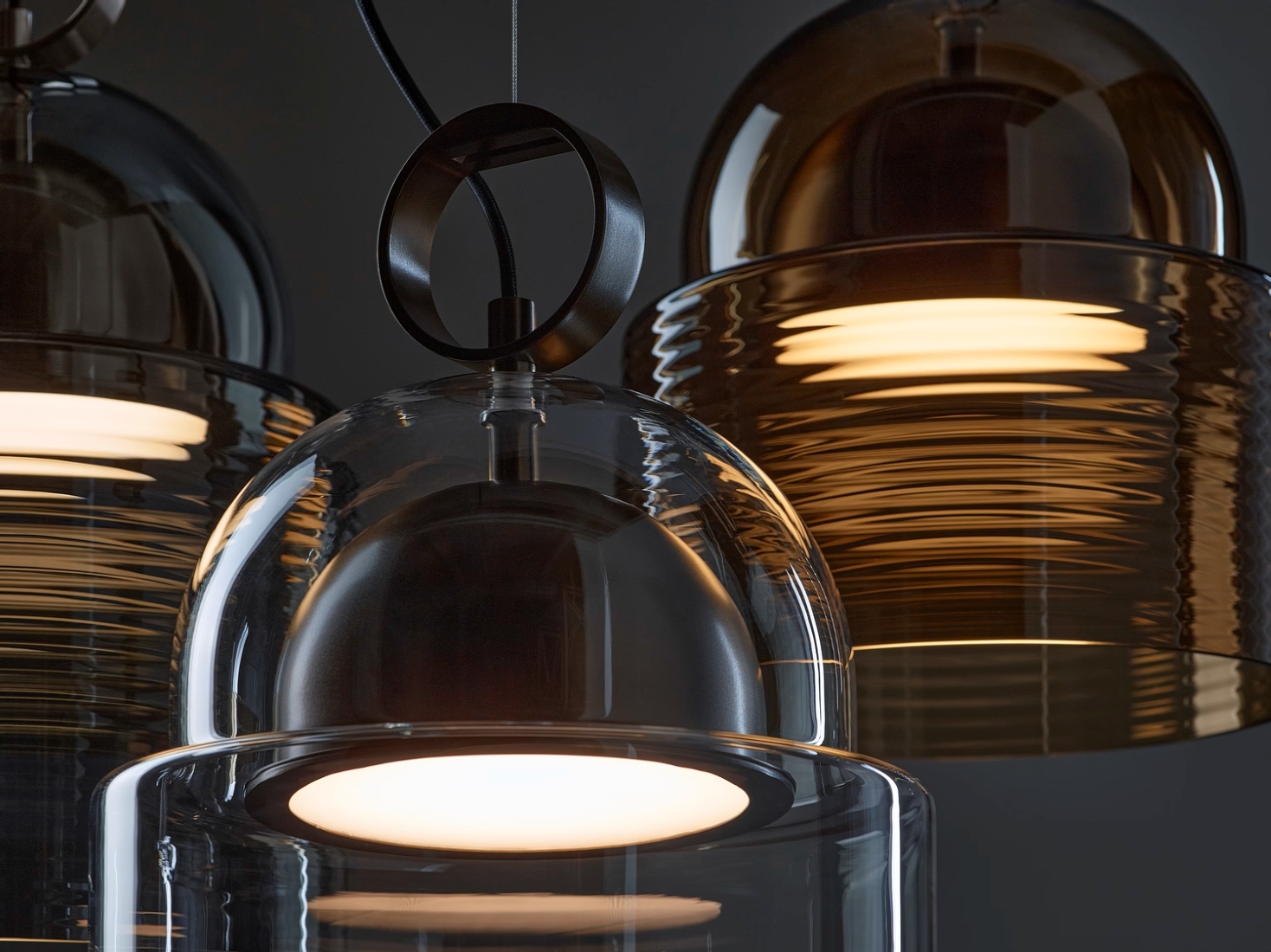 Brokis Dome pendant lights; smoke brown and clear domes emit a warm, elegant glow against a dark backdrop.