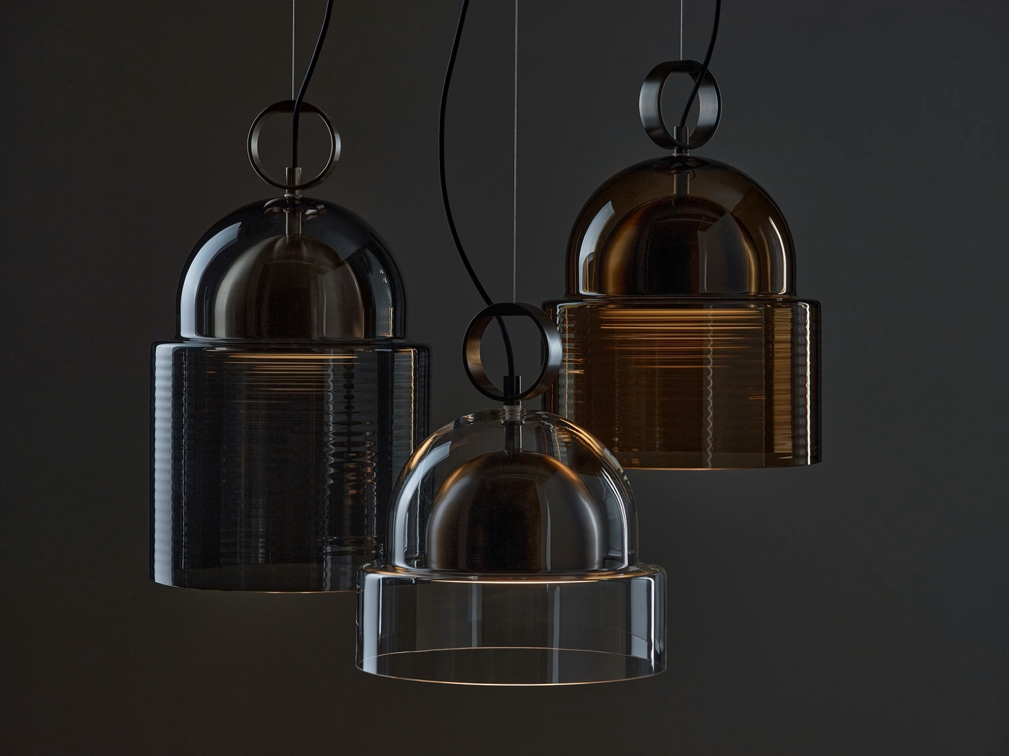 Trio of sculptural Brokis Dome pendants in smoke grey, brown, and transparent glass glow against a moody backdrop.
