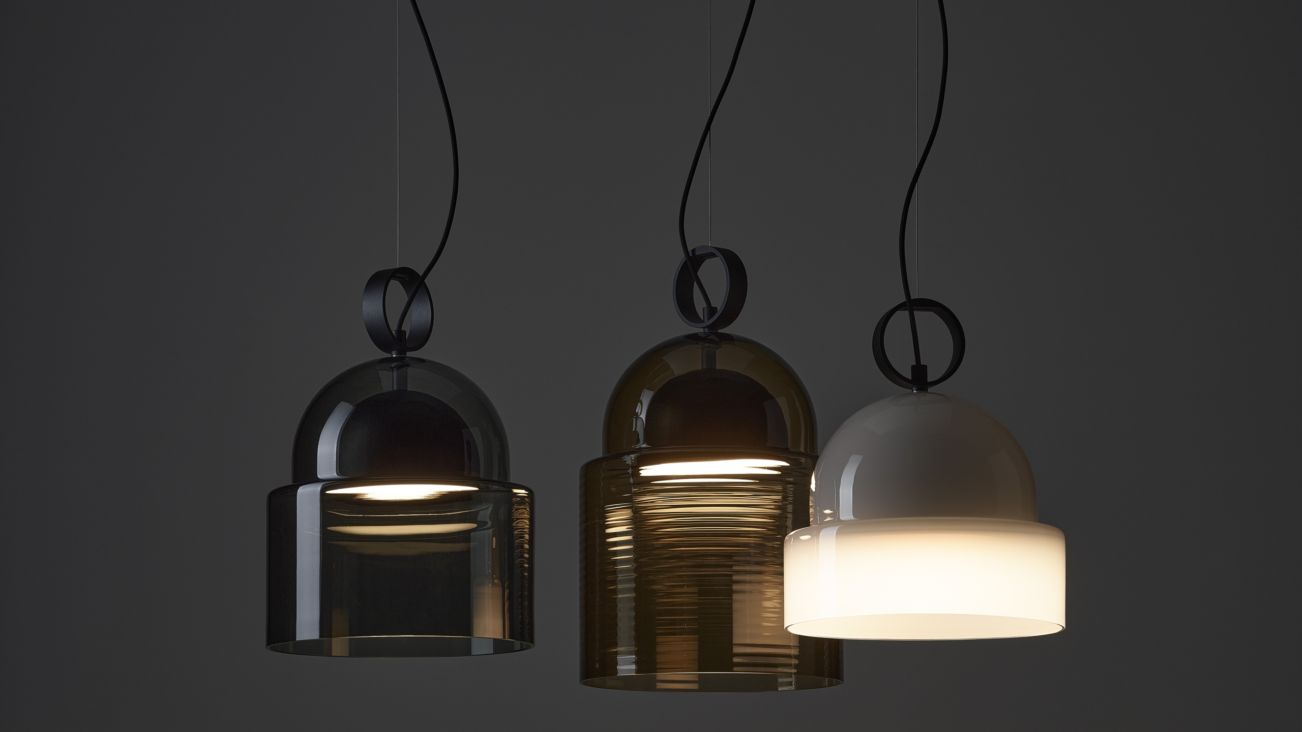 Three Brokis Dome pendants with hand-blown glass - smoky grey, ribbed brown, and opaline - float against a dark backdrop.