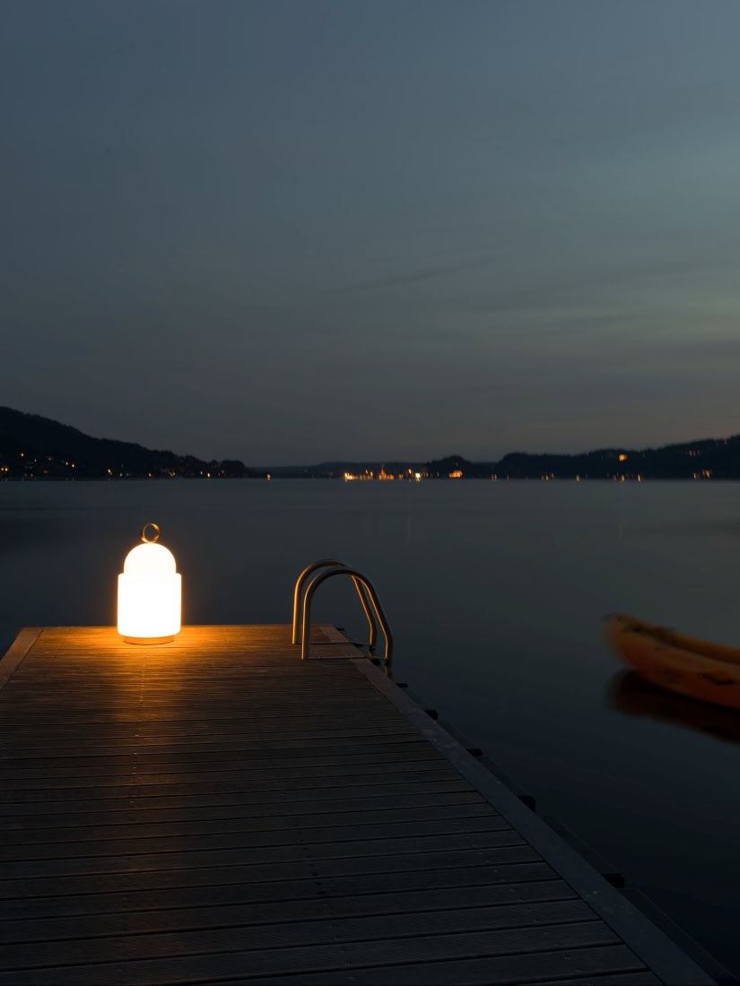 Brokis Dome Nomad Large glows on a wooden jetty above a tranquil dusk lake, with hills and lights beyond.