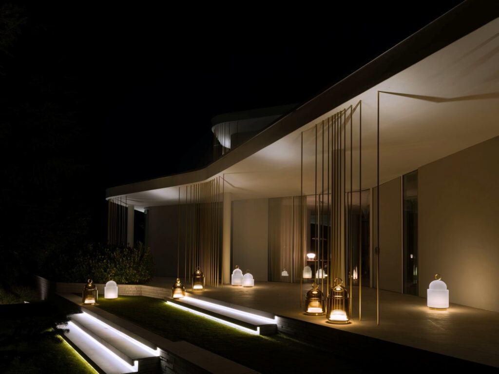 A modern building at night, its angular white roof and glass façade illuminated by Brokis Dome Nomads along wide steps.