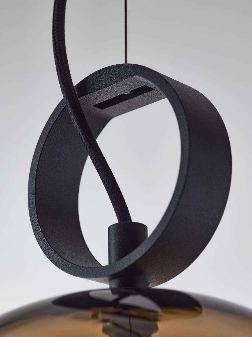 Close-up of a black metal Brokis Dome Pendant with a circular loop and textured flex, atop a handblown brown glass shade.