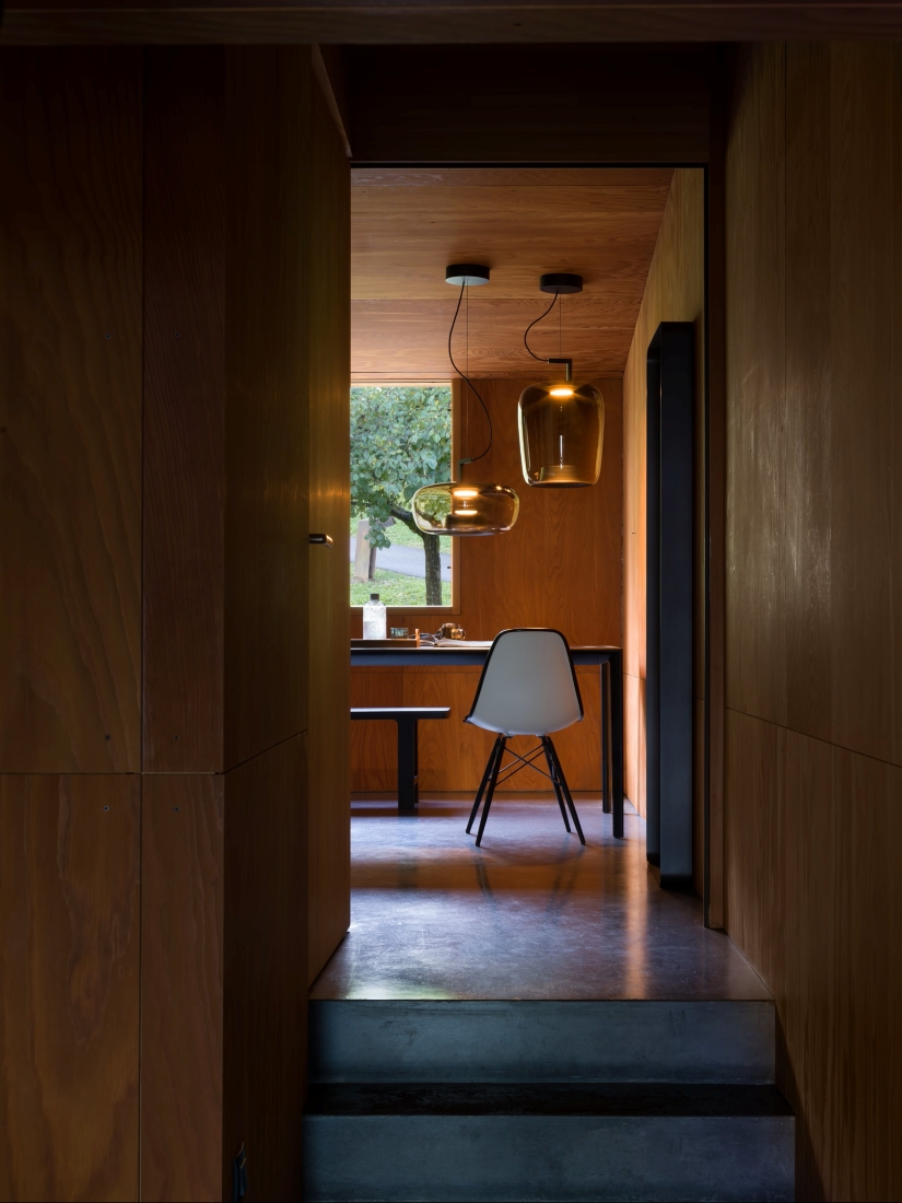 A minimalist wooden interior leads to a dining area with Brokis Double pendants over a black table and white chair.