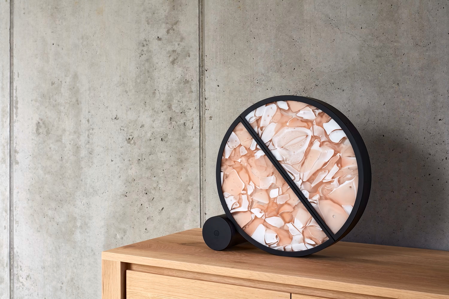 A Brokis Geomotric Table with a black frame and pink BROKISGLASS face leans on a cupboard against concrete.