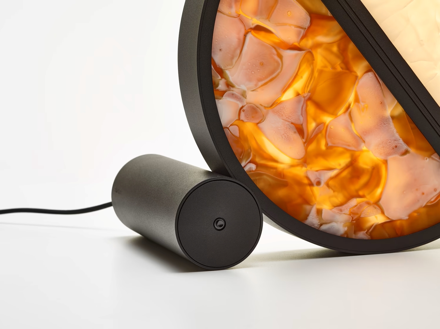 A cylindrical black power adaptor connects to a Brokis Geometric Table lamp, its cognac BROKISGLASS on a white backdrop.