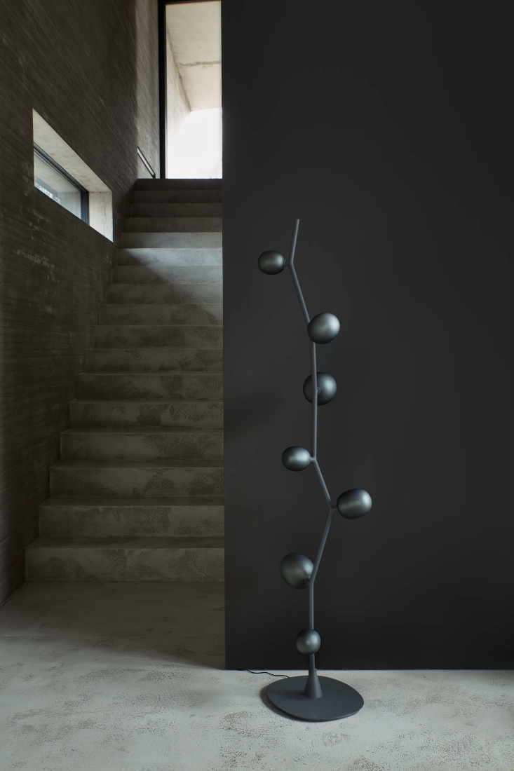 A luxurious minimalist space with concrete stairs, dark wall, and a Brokis Ivy Floor lamp. Natural light streams in.
