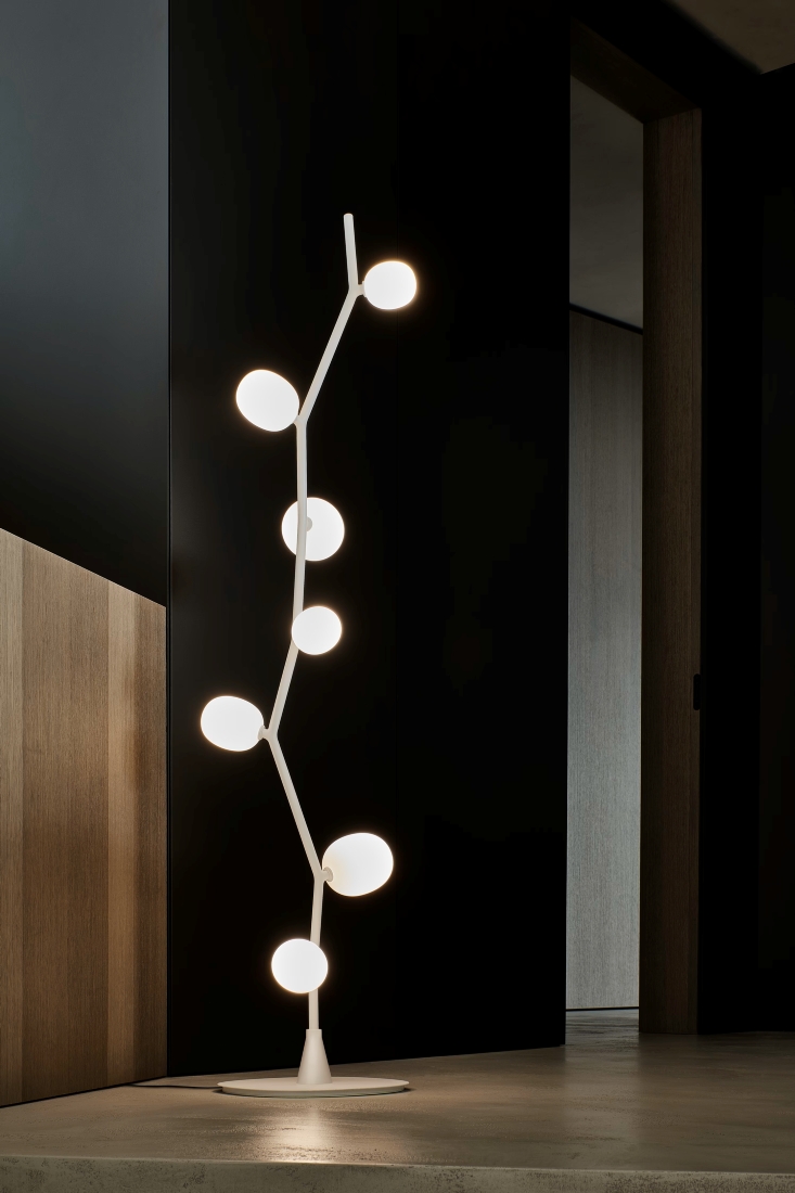 White Brokis Ivy Floor lamp with six glowing orbs stands on concrete, elevating a minimalist room’s luxury aesthetic.