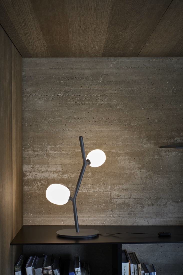 Brokis Ivy Table lamp with glowing crystal globes graces a black shelf, set against warm concrete and timber walls.