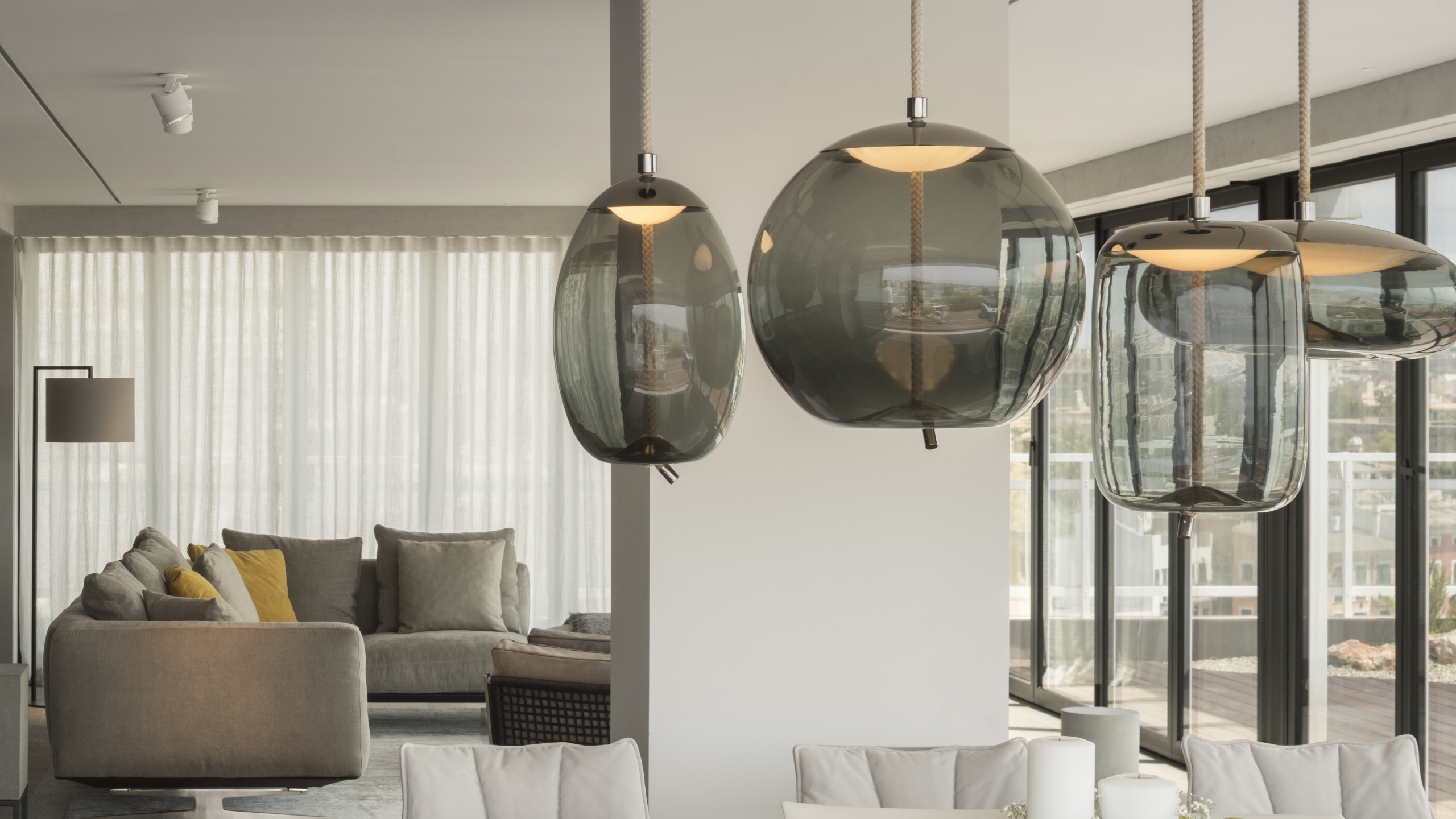 Brokis Knot pendants in a modern living room with plush neutral sofas, and sheer curtains in sunlight.