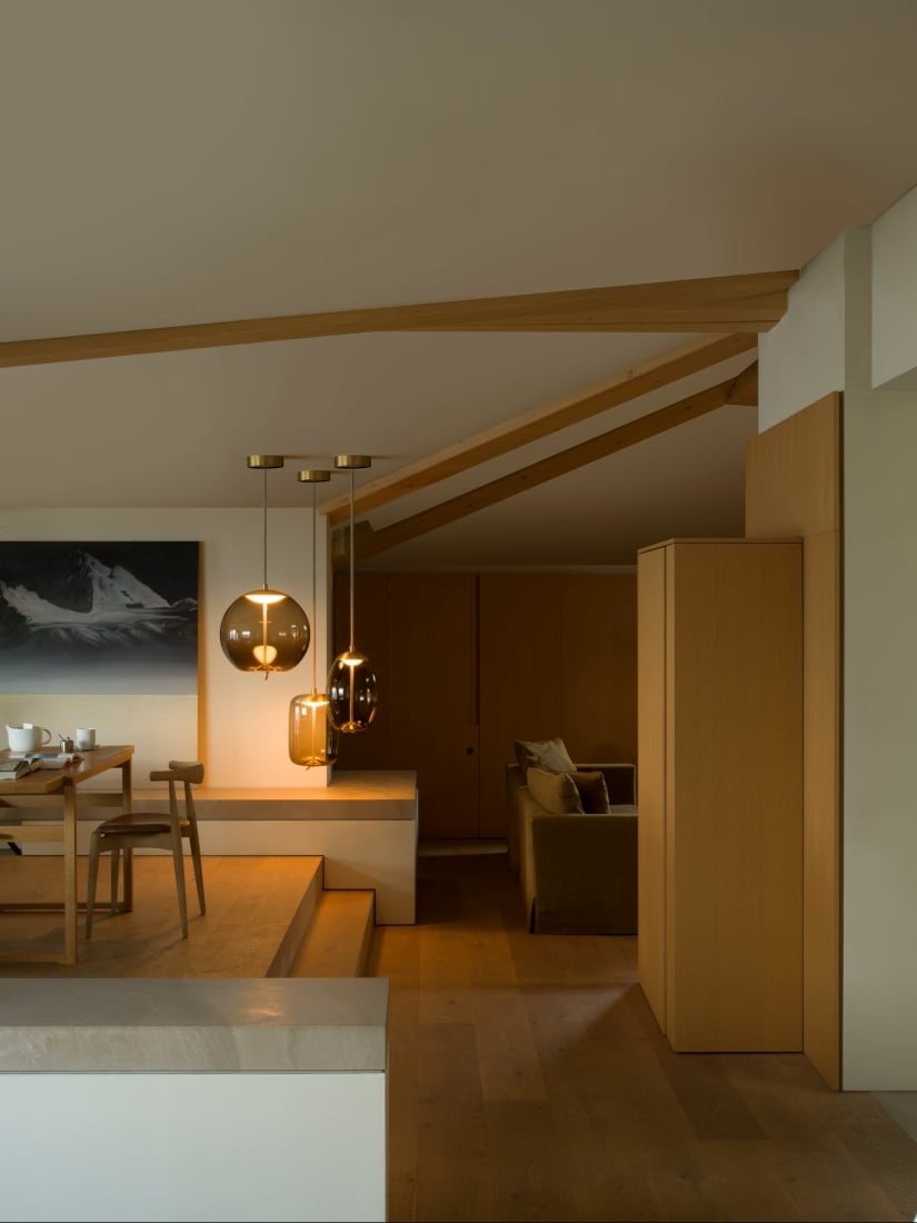 Modern living space with warm wooden floors, Brokis Knot Pendants above dining, and serene mountain artwork.