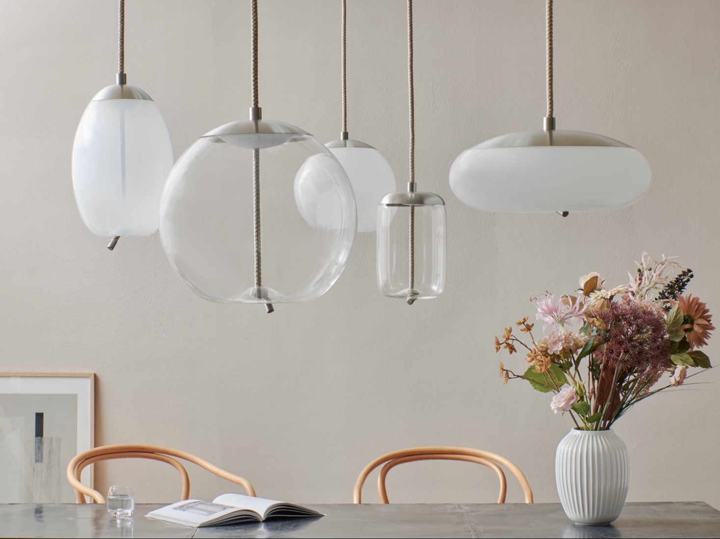Brokis Knot Small pendants elevate a minimalist table with a ceramic vase, pastel blooms, and airy wooden chairs.
