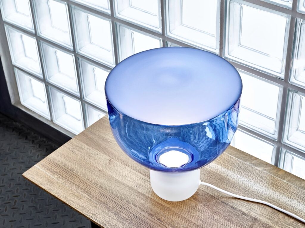 Brokis Lightline S Table lamp with a frosted base and sculptural blue glass shade glows atop a luxurious wooden table.
