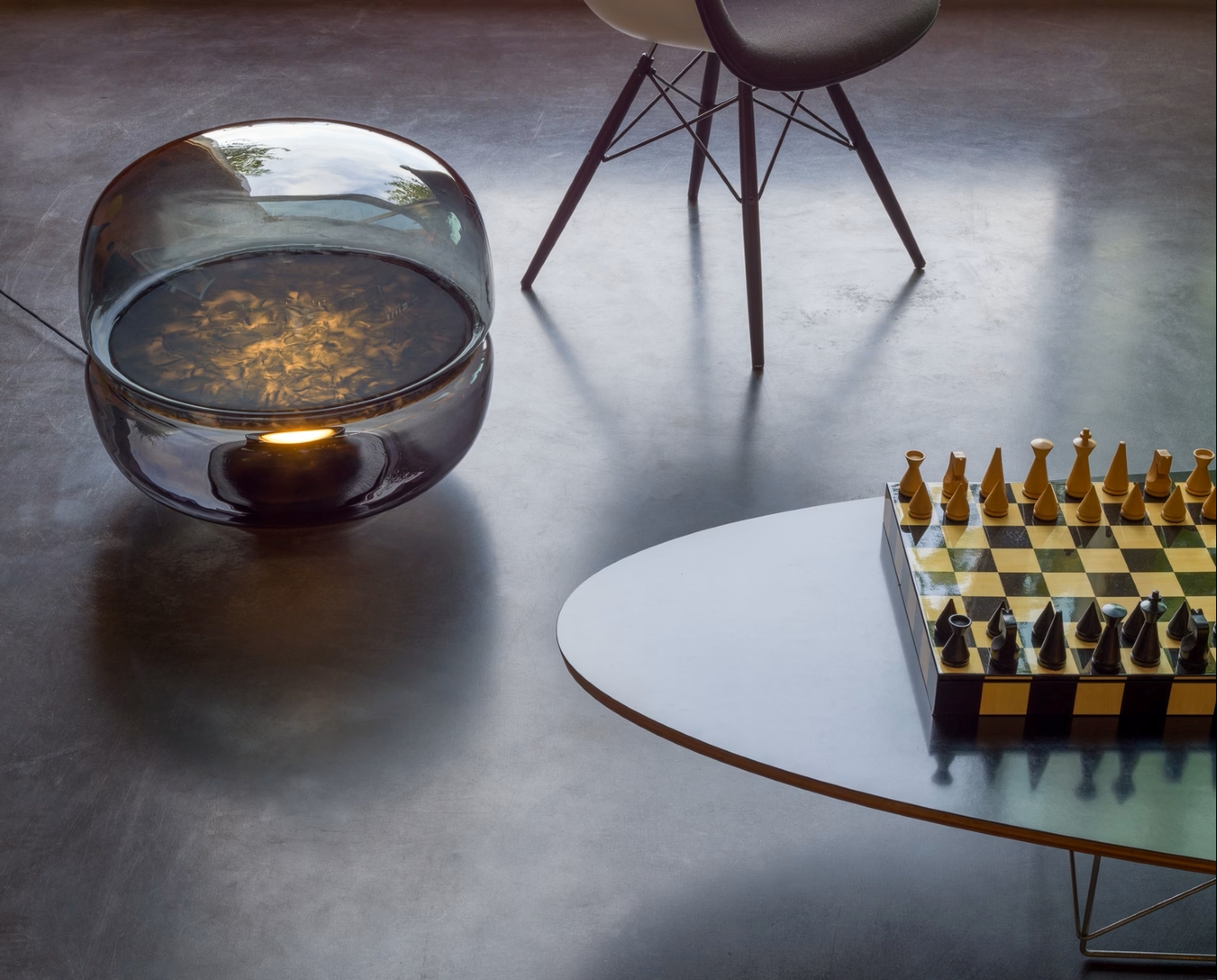 Brokis Macaron L lamp graces a grey floor beside a black chair and an oval table with a luxe chessboard.
