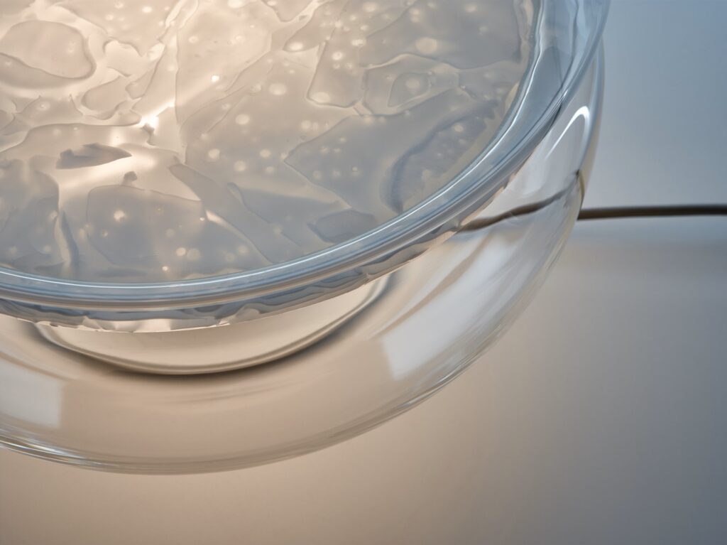 A close-up of Brokis Macaron M lamp diffusing soft light through BROKSGLASS, cord elegantly trailing below.