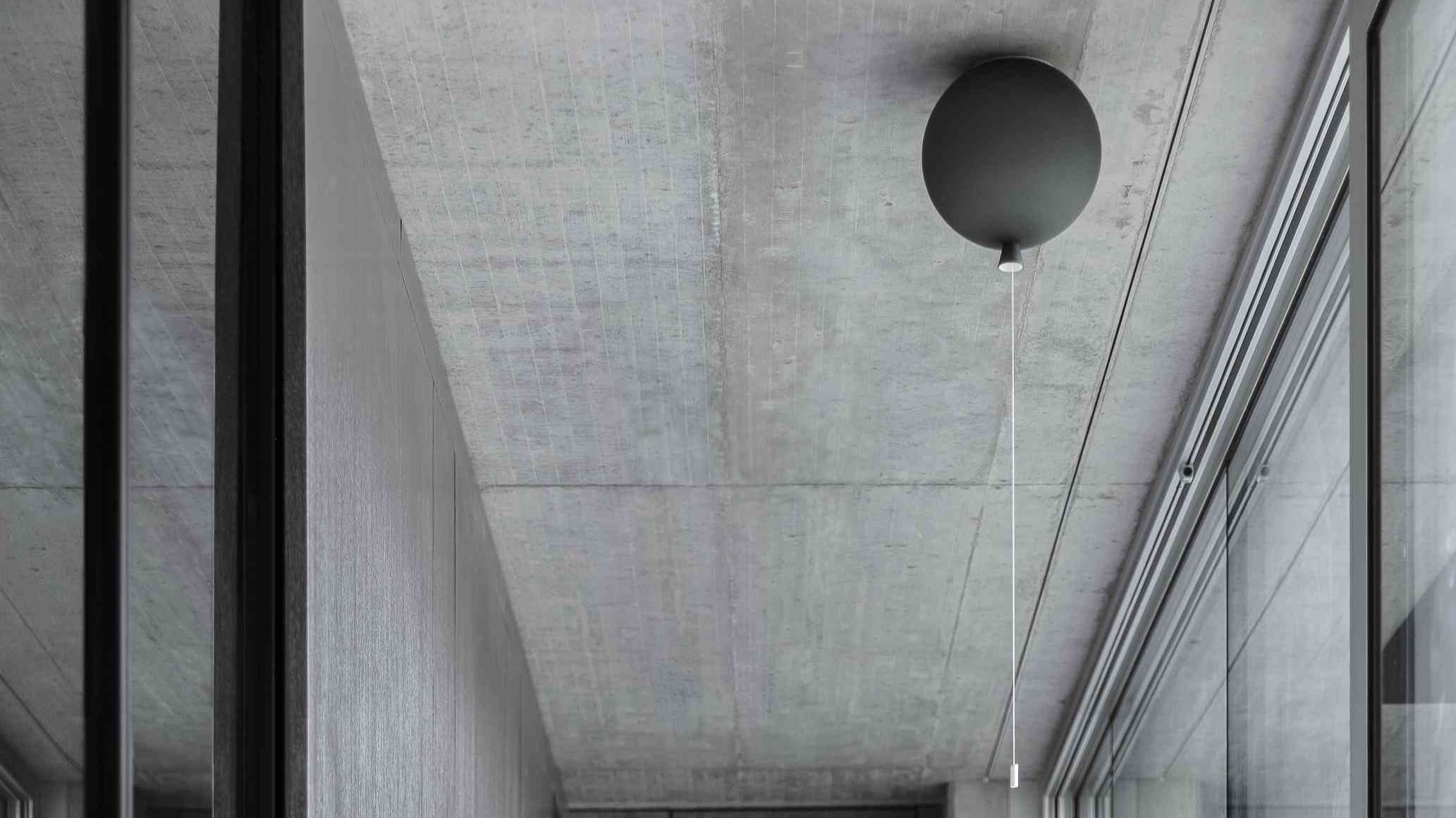 Brokis Memory ceiling light with a round black glass and pull cord hangs from concrete above full-height glass windows.