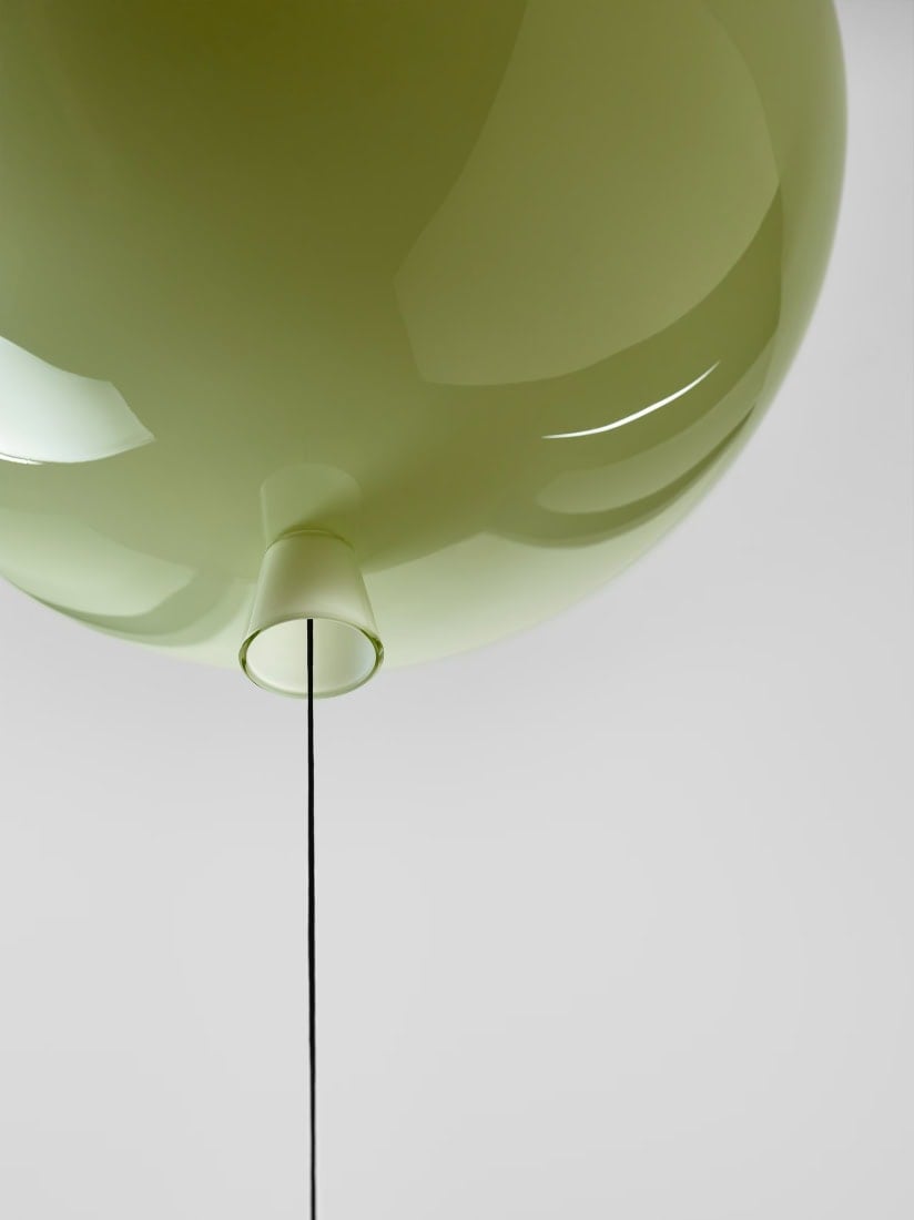 An olive green spherical Brokis Memory light with a cord, its smooth glass surface gleaming against a light grey backdrop.