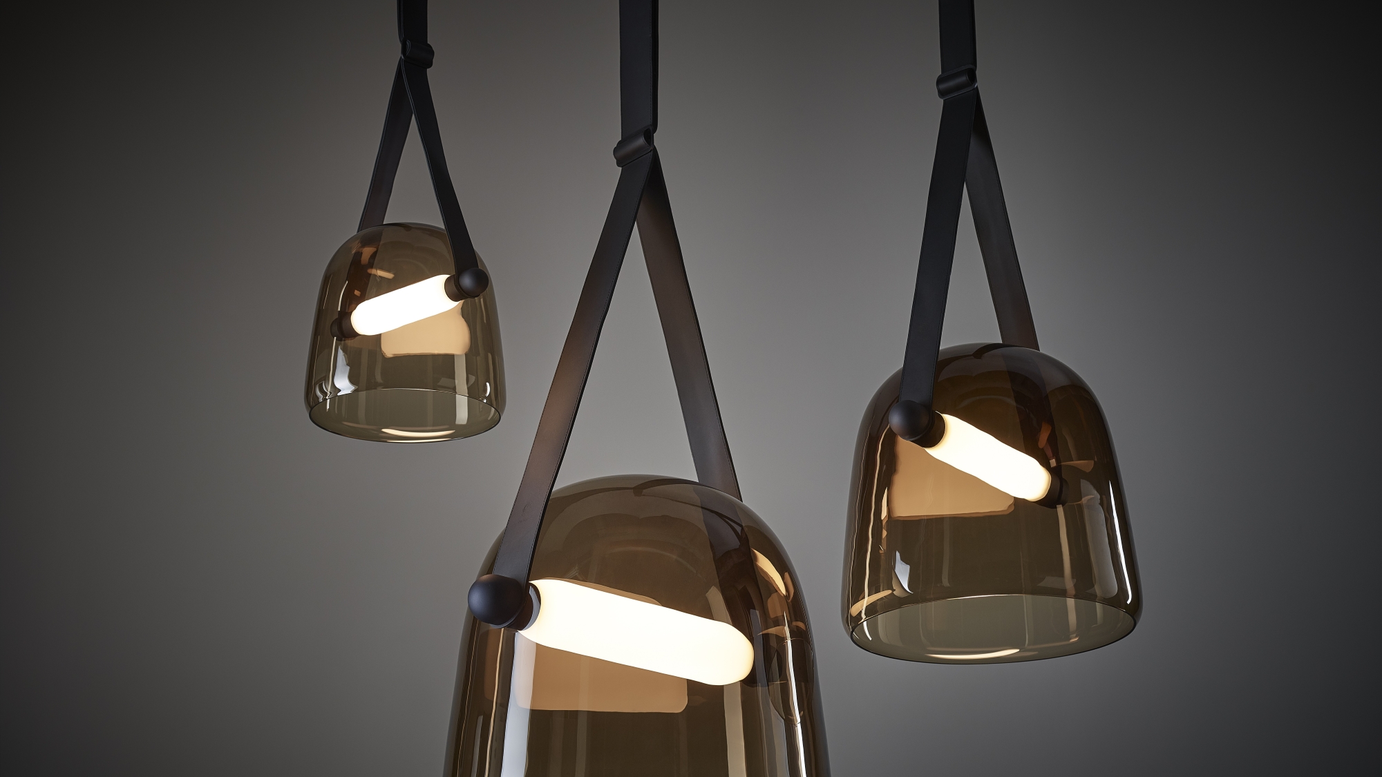 Brokis Mona pendants in smoke brown glass, each with a luminous white LED tube, hang elegantly at varied heights.