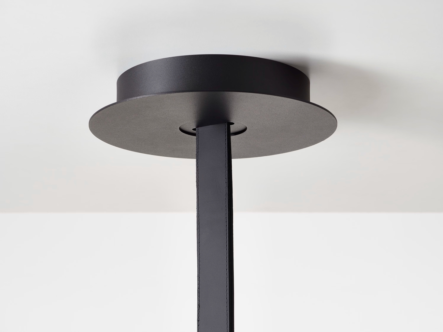 A close-up of a Brokis Mona ceiling canopy with a matt black base and leather, accenting the luxurious, minimal décor.