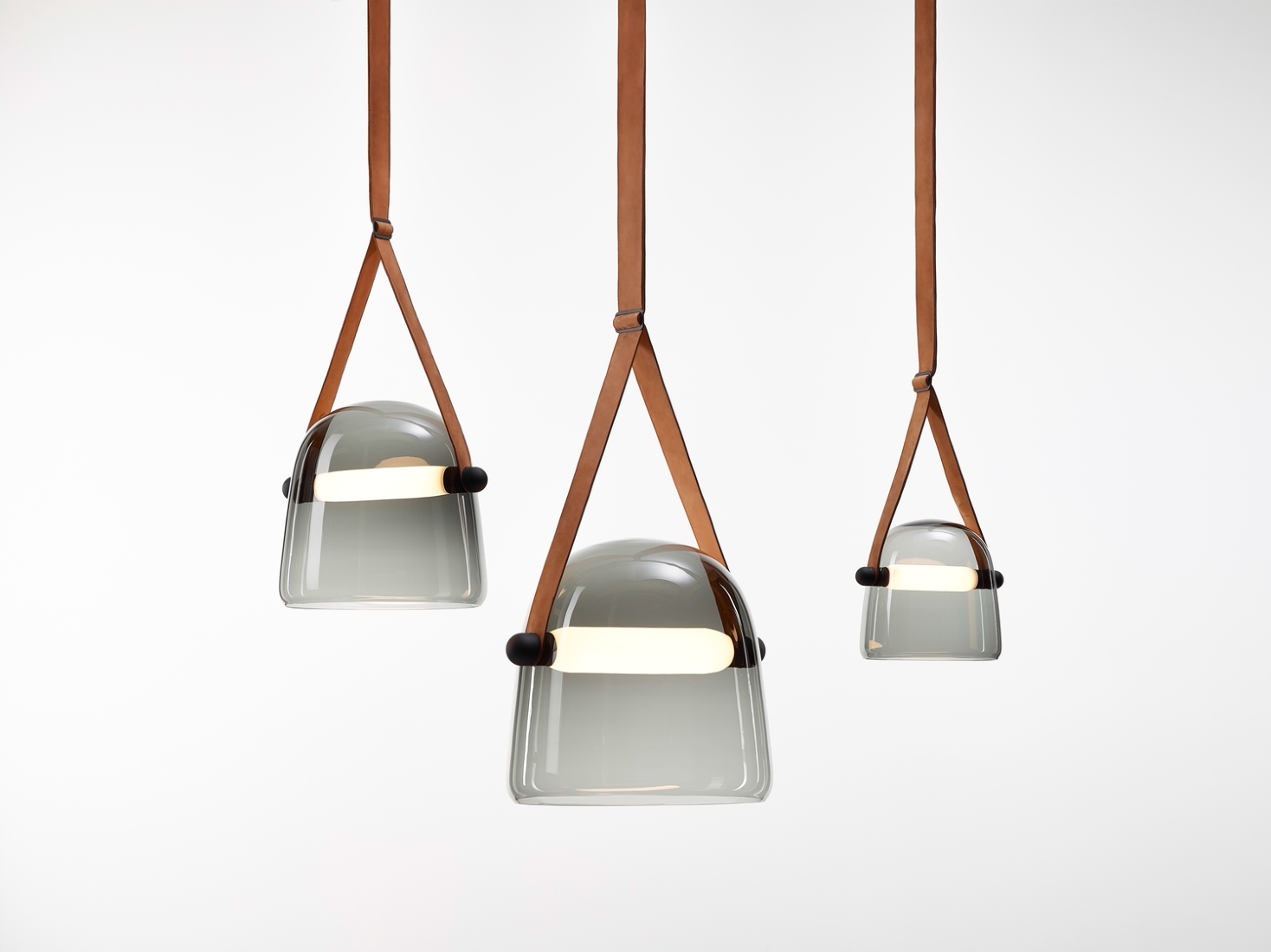 Brokis Mona pendants with handblown grey glass domes suspended by tan leather straps in graduated sizes.