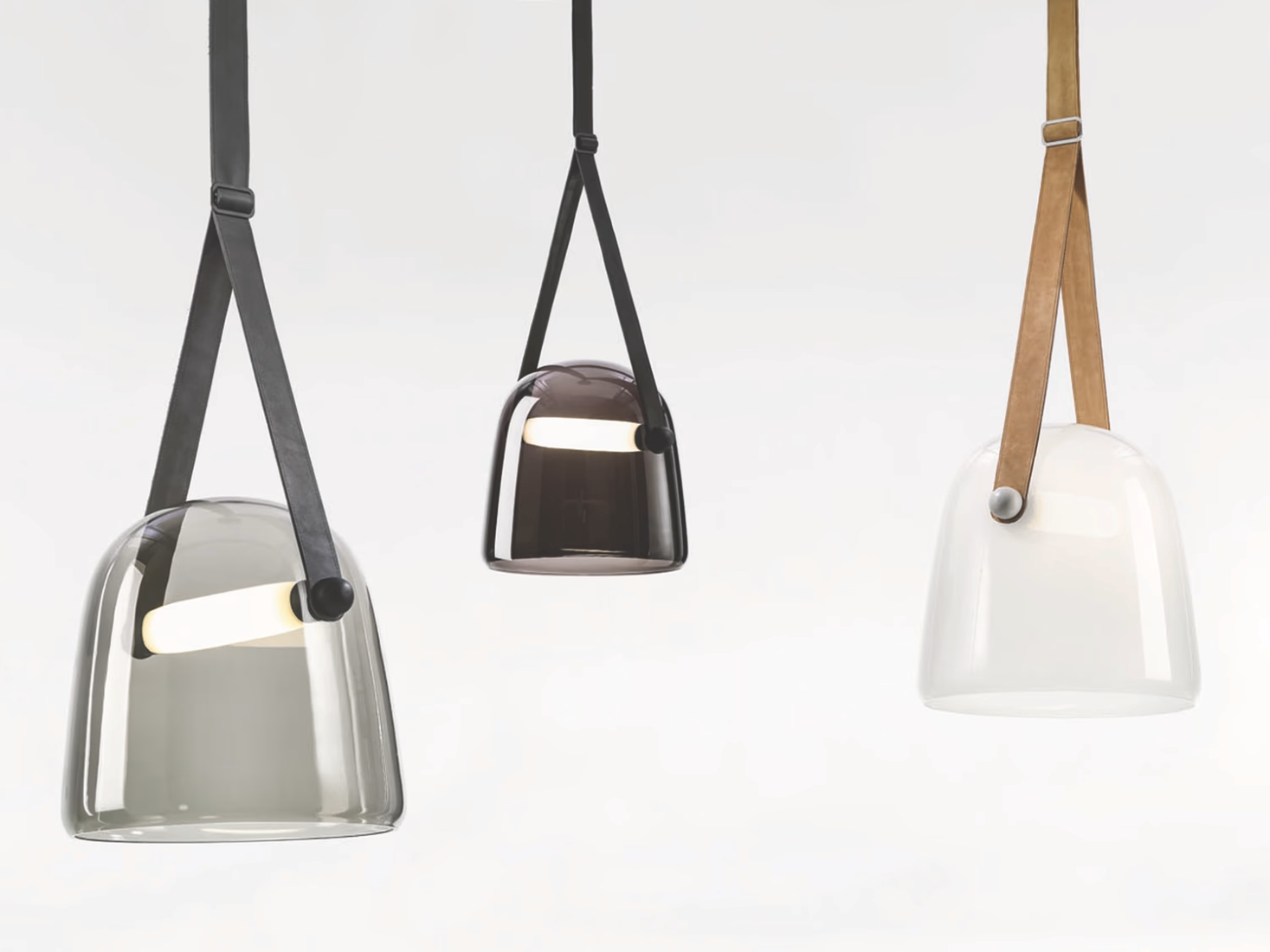 Brokis Mona pendants in handblown glass - grey, black, white - hang from luxe leather straps on a crisp white backdrop.