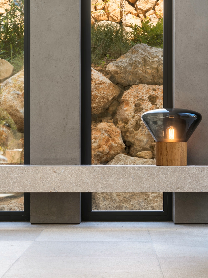 Brokis Muffins Wood 02 with wood base and glass shade graces a stone ledge by tall windows, radiating refined minimalism.