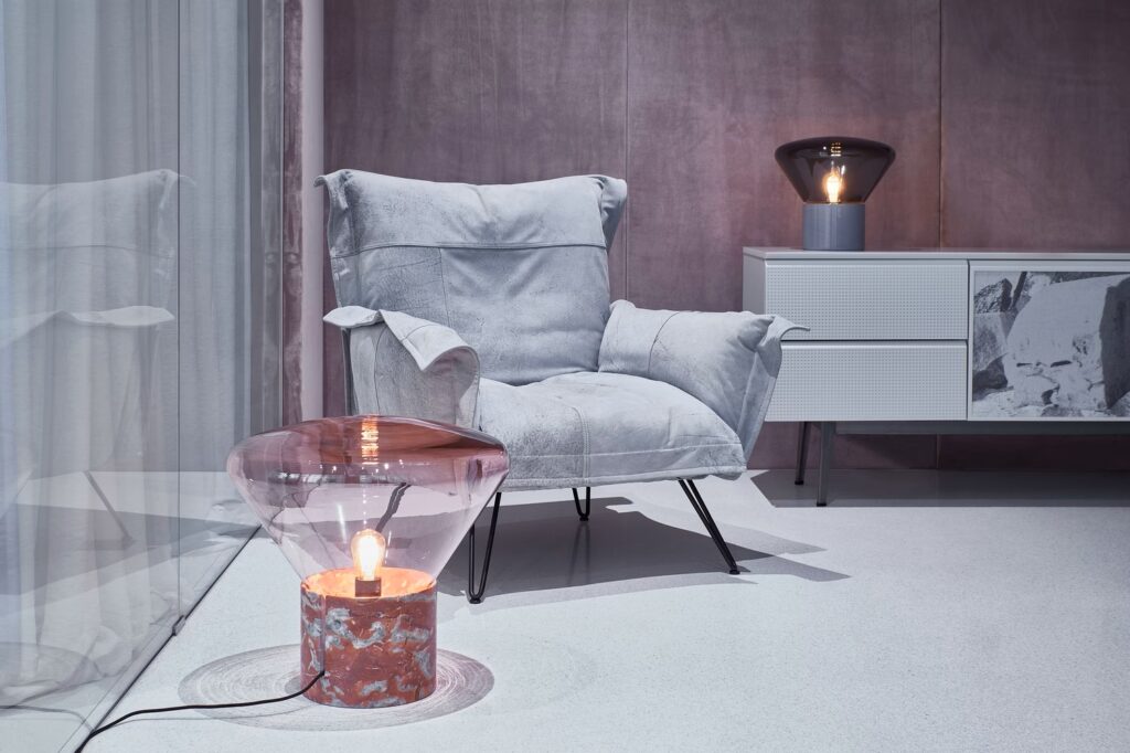 A modern room with a plush grey armchair, side table and marble Brokis Muffins Table lamps against mauve walls.