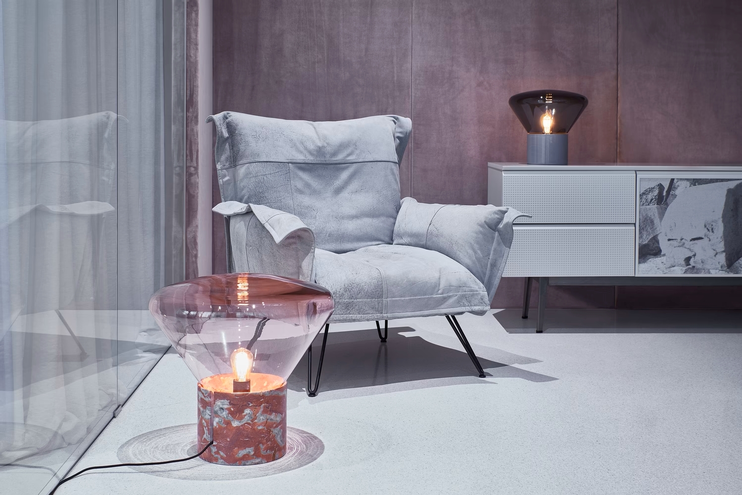 A modern room with a plush grey armchair, side table and marble Brokis Muffins Table lamps against mauve walls.