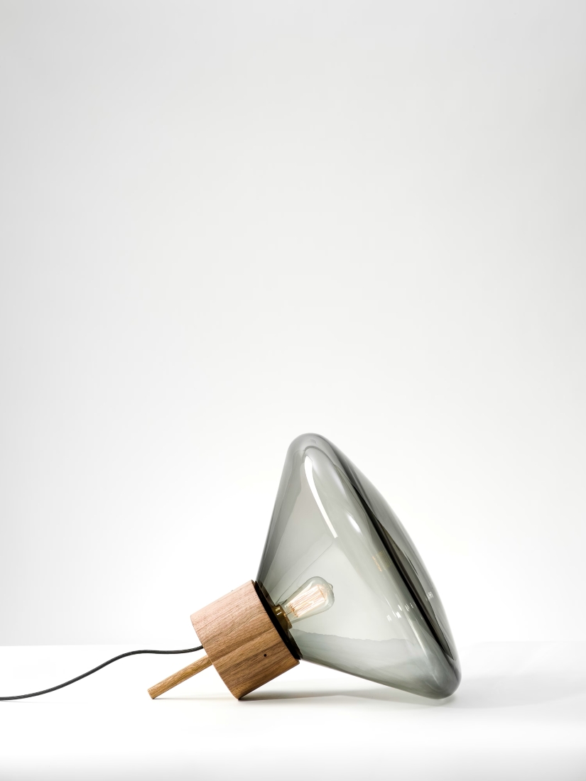 Brokis Muffins Wood 03A lamp with handblown glass shade and exposed bulb rests artfully on a white surface, lead trailing.