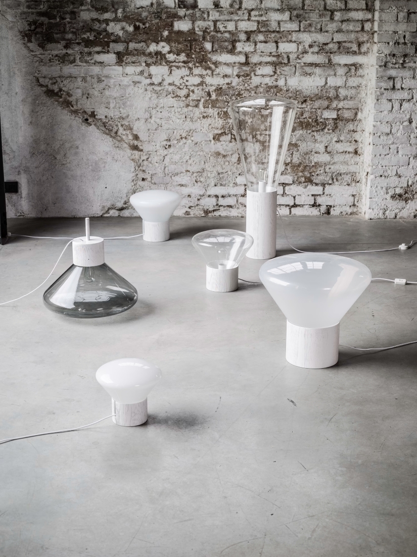 Brokis Muffins table lamps with glass and white opaline glass tops rest on concrete by a whitewashed brick wall.