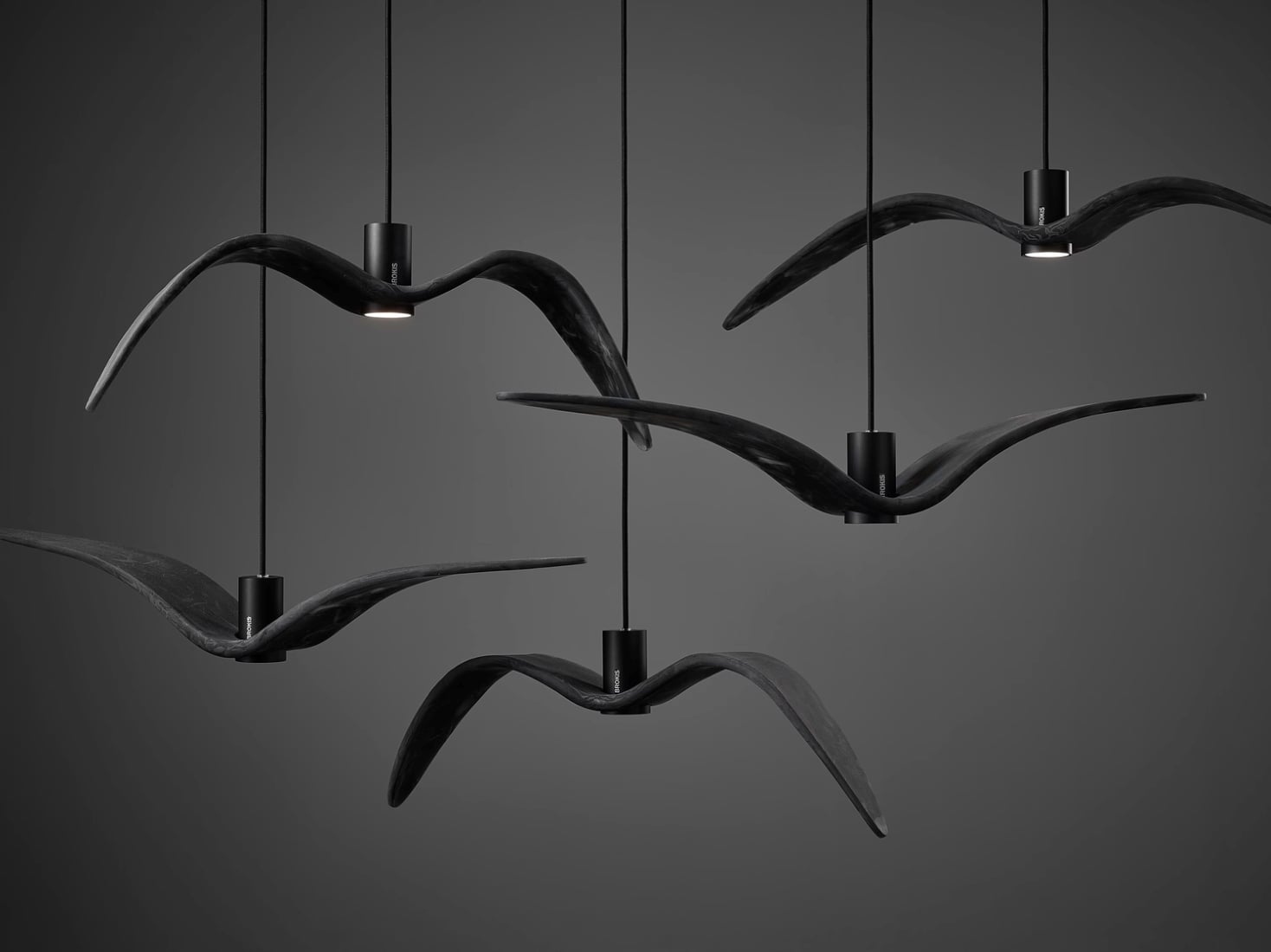 Brokis Night Birds pendant lights with winged silhouettes glow elegantly against a dark grey backdrop.