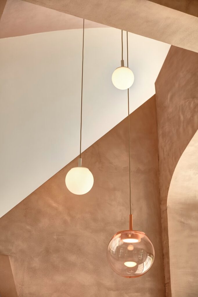 Brokis Orbis 300 pendant in light pink glass float against Sfera pendants among textured peach geometric walls.