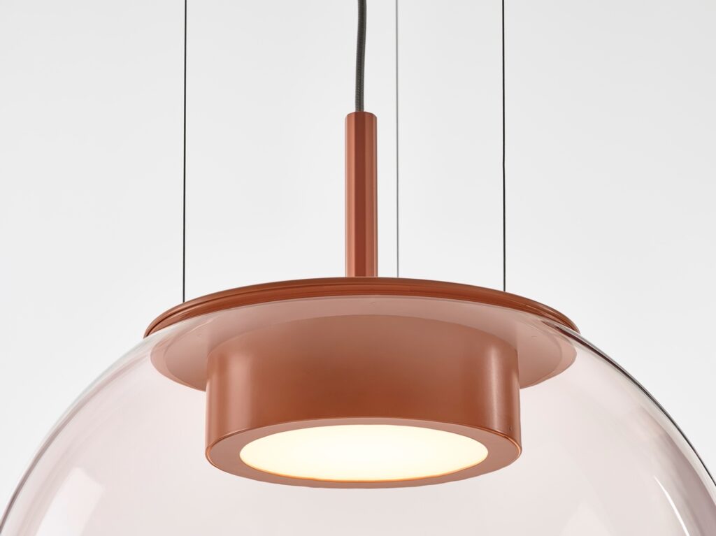 A close-up of a Brokis Orbis 150 pendant with hand-blown light pink glass, suspended by slender cables.