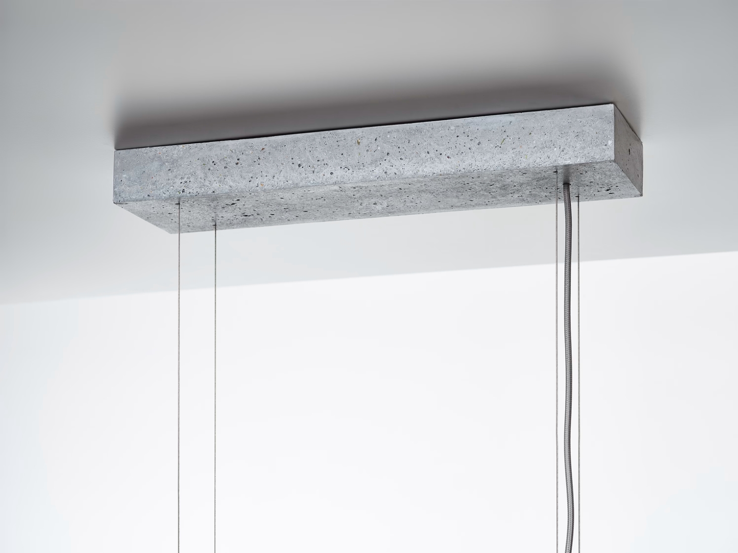 Brokis Overlay Chandelier concrete canopy is suspended from a white ceiling with thin cables and matching electrical cords.