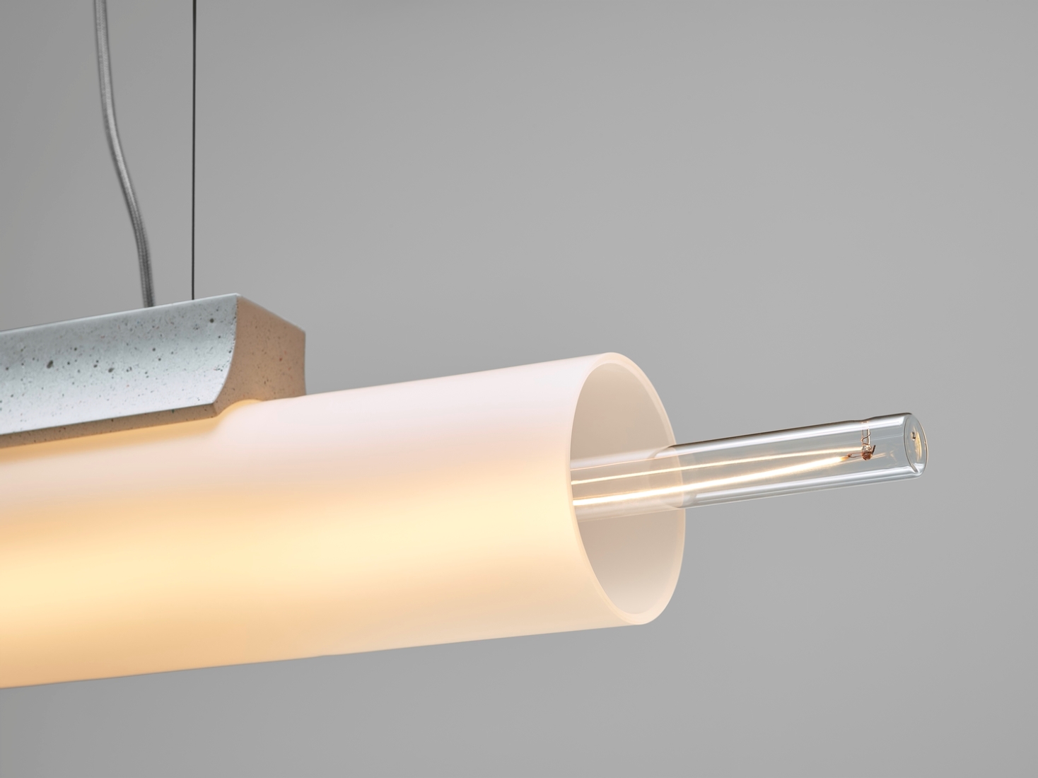 A close-up of a Brokis Overlay Chandelier L with handblown glass shade and glowing filament, against a soft grey backdrop.