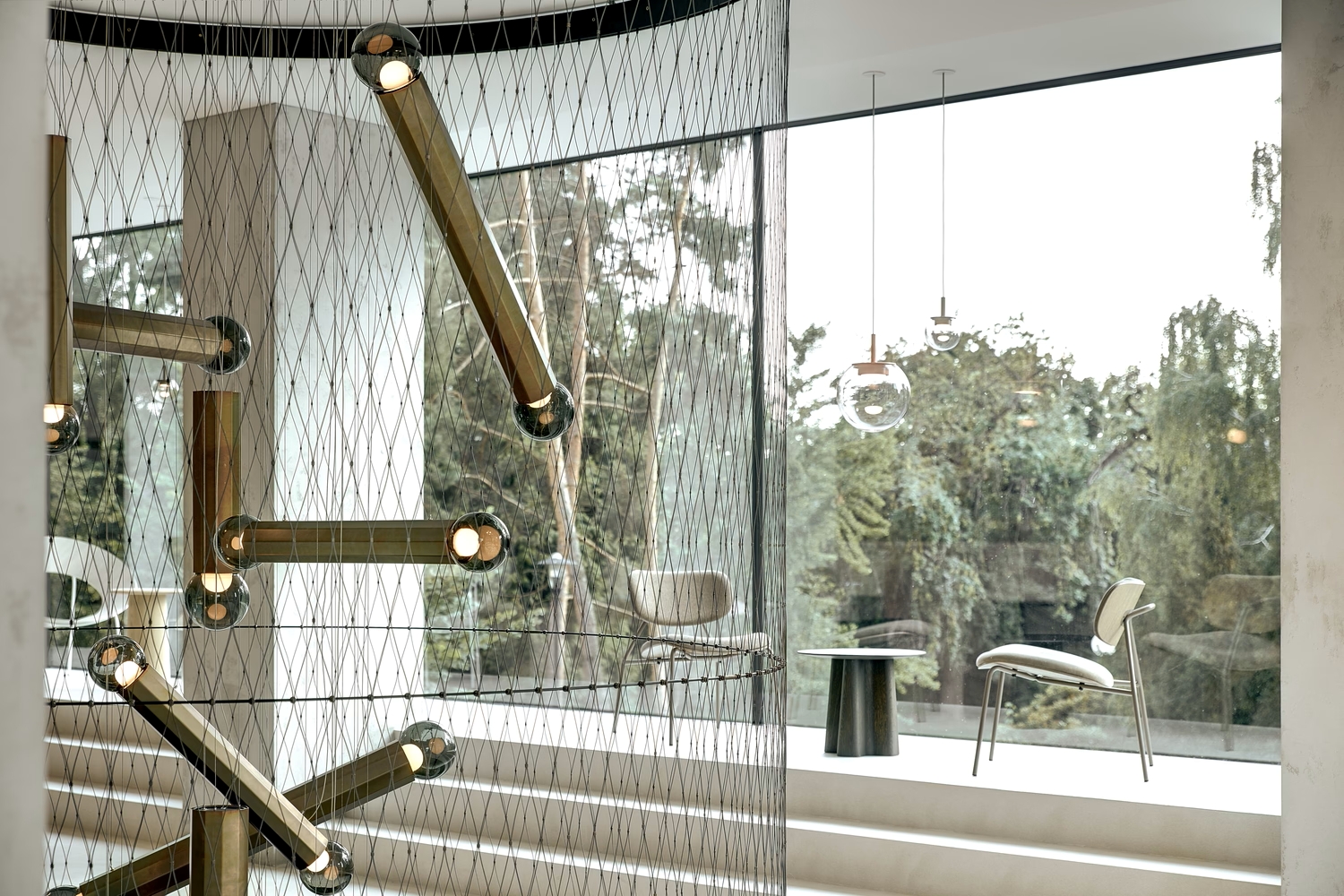 Luxury interior with soaring windows framing lush trees, Brokis Prisma chandelier, white steps, and elegant seating.