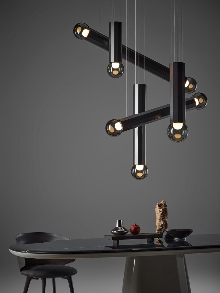 A modern dining area with a glossy black table, single chair, and Brokis Prisma lights glowing above a grey wall.