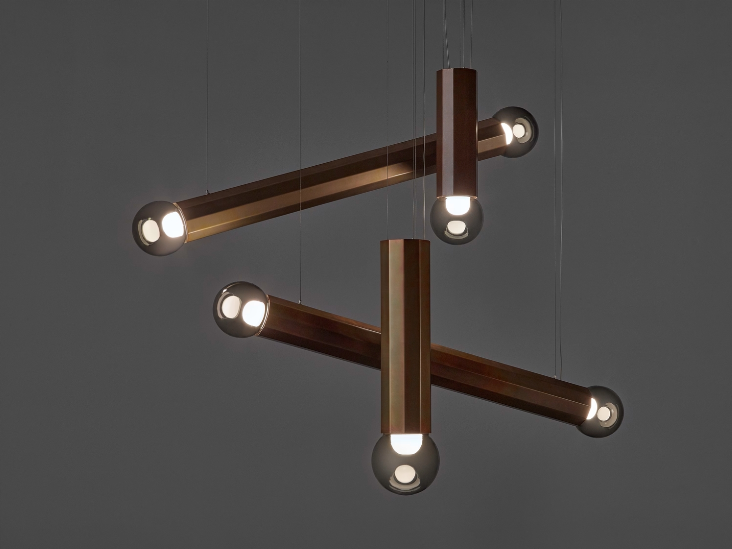 Brokis Prisma pendants with handblown glass globes and zinc rods, floating elegantly against a dark backdrop.