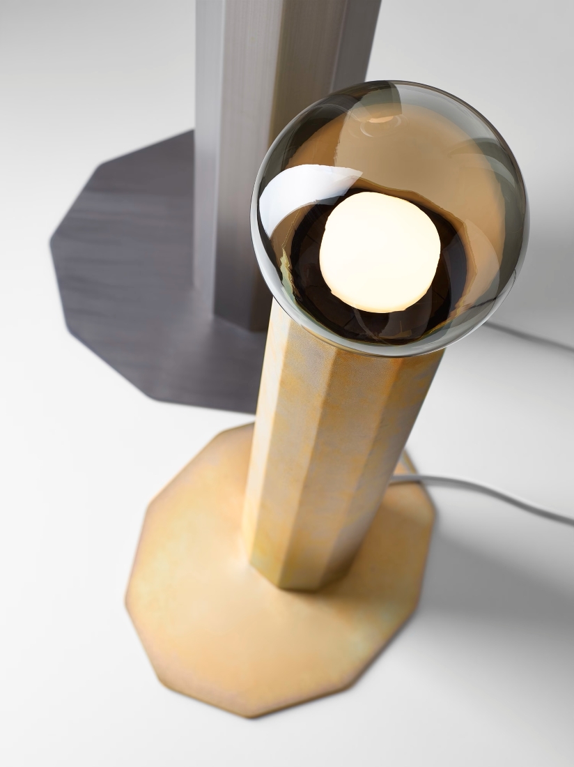 Luxurious close-up of two Brokis Prisma floor lamps with handblown glass globes, zinc and steel geometric bases on white.
