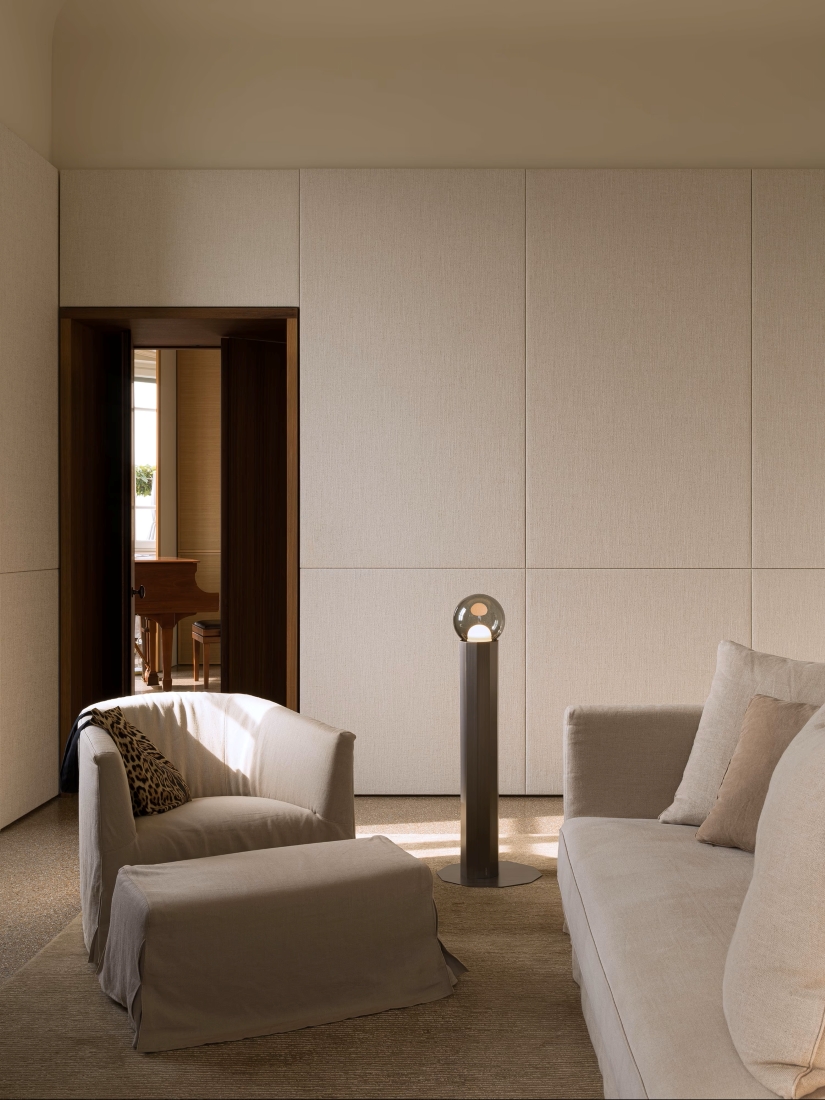 A living room with beige walls, a grey sofa, and an armchair, with a Brokis Prisma Floor Large 800 between them.