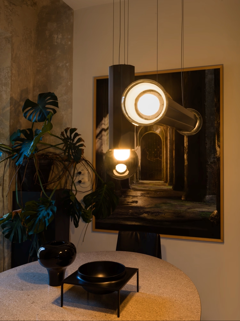 A modern dining area with a round table, black ceramic bowls, Brokis Prisma pendant lights, and sleek artwork.